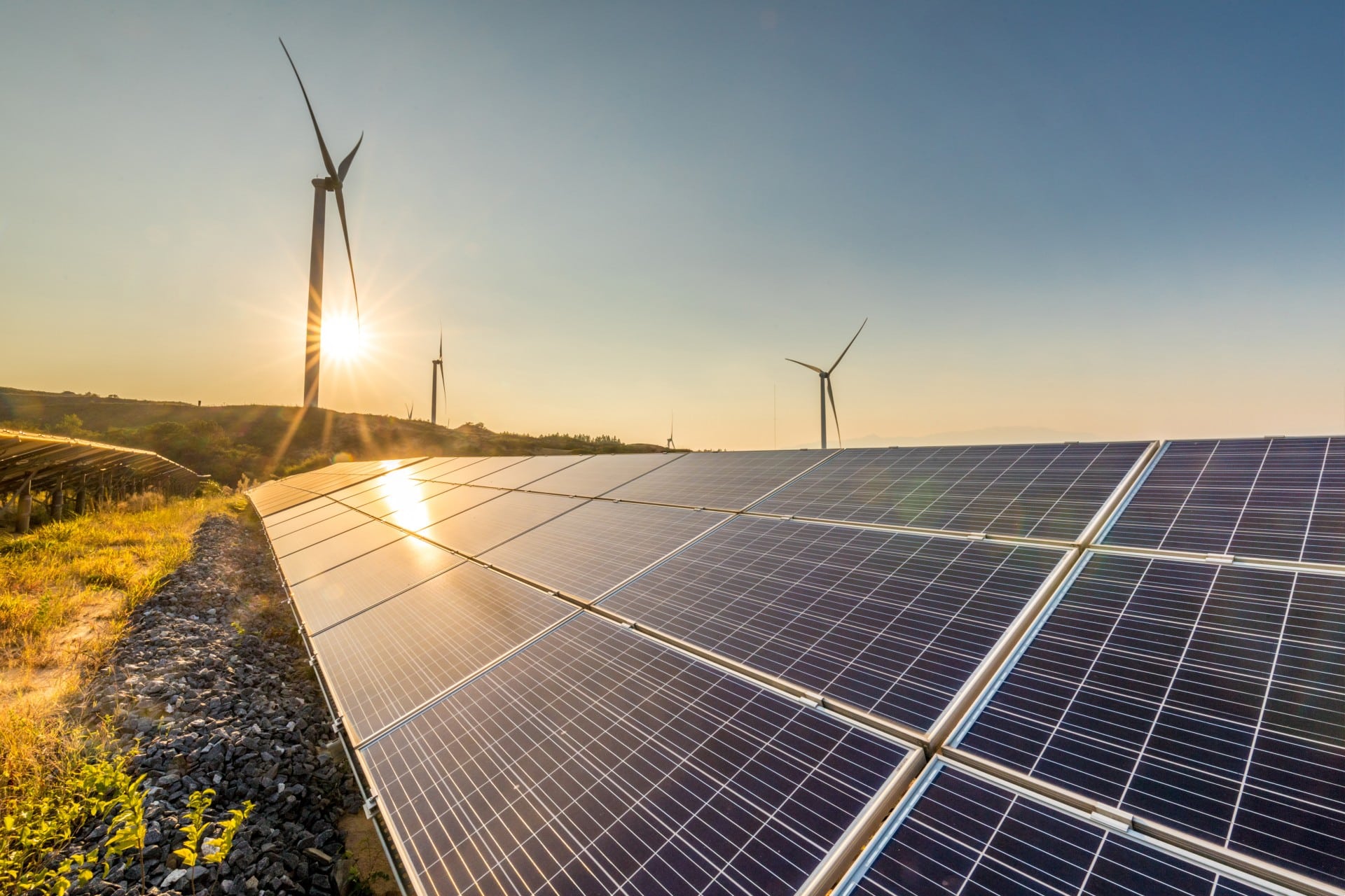 Solar photovoltaic panels at sunrise beside wind turbines
